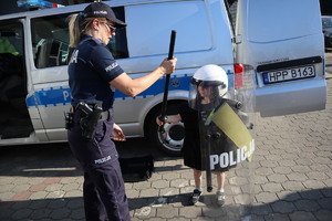 Policjantka pomagająca dziecku przymierzyć policyjną kamizelkę oraz kask