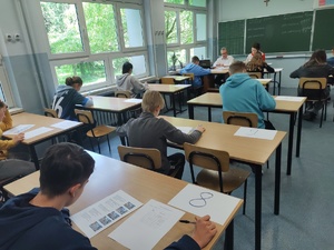 Na zdjęciu uczniowie siedzący przy ławkach, piszący test.