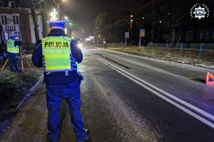 Miejsce wypadku drogowego. Jezdnia, radiowóz i pracujący na miejscu policjanci.