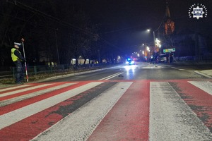 Miejsce wypadku drogowego. Jezdnia, radiowóz i pracujący na miejscu policjanci.