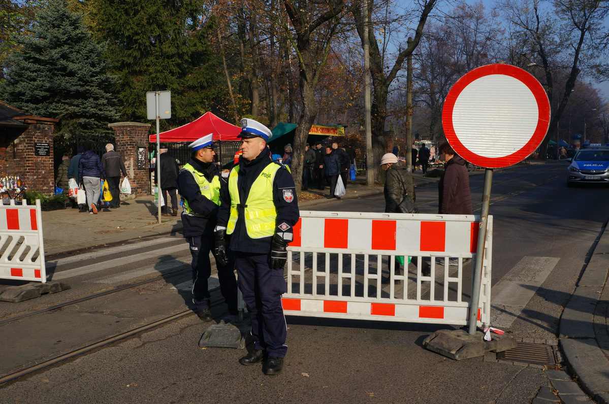 Policjanci ruchu drogowego zabezpieczają jezdnię przy cmentarzu.