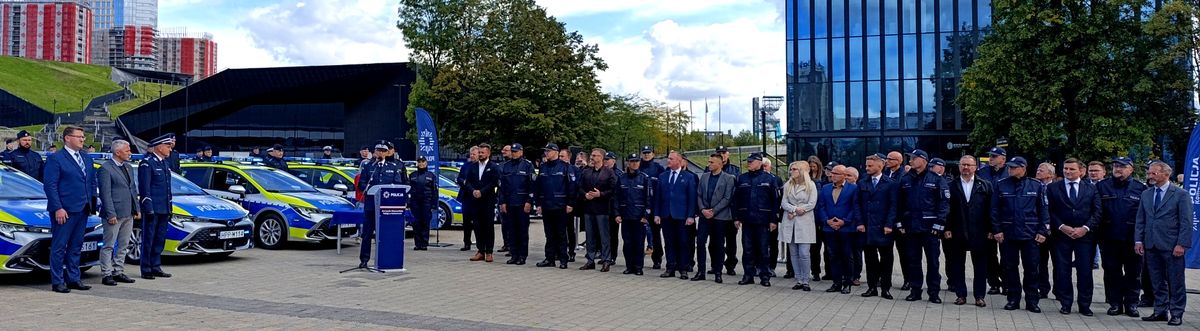 Na zdjęciu umundurowani policjanci stojący przy radiowozach służbowych