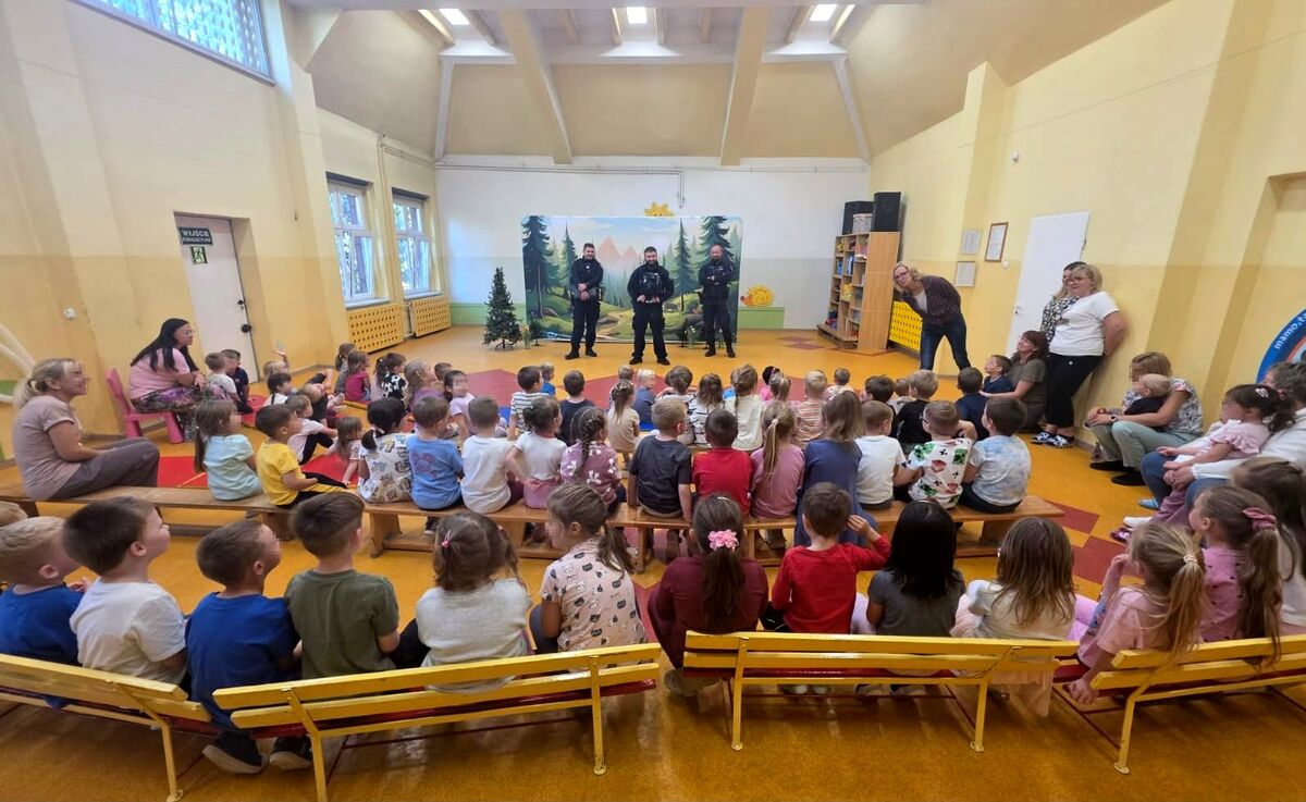 trzech policjantów stojących w sali przed dziećmi 