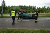 Policjant podchodzi do uszkodzonego auta, strażacy sprzątają szkoło z jego szyb.