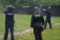 Dwóch policjantów strzela do tarczy pod okiem instruktora.