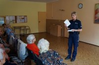 Policjantka omawia seniorom ulotkę z informacjami dotyczącymi ich bezpieczeństwa