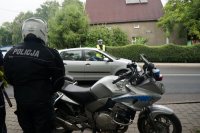 Motor policyjny a przy nim mundurowy przygotowany do jazdy nim, w tle policjant kontroluje stan trzeźwości kierowcy osobówki