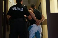 Policjantka prowadzi zatrzymanego w kajadnakach