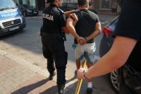 Policjantka prowadzi zatrzymanego w kajadnakach