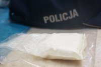 Woreczek strunowy z substancją koloru białego, w tle policyjna czapeczka z daszkiem