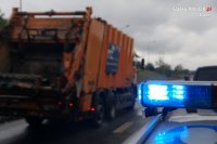 Policyjny sygnalizator na dachu radiowozu a w tle jadąca śmieciarka