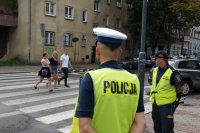 policjant obserwuje jak przez jezdnię przechodzą piesi