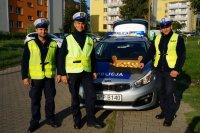 trzech policjantów stoi przy radiowozie