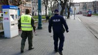 policjant wraz z żołnierzem patroluje przystanek tramwajowy