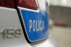 Zdjęcie przedstawia fragment radiowozu policyjnego z napisem Policja