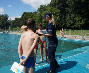 policjantka rozdaje książeczki edukacyjne chłopcom na basenie