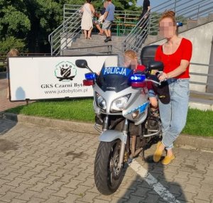 dziecko na motorze policyjnym i stojąca obok kobieta