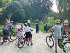 Policjantka w parku prowadzi rozmowę z rowerzystami na temat bezpiecznej jazdy