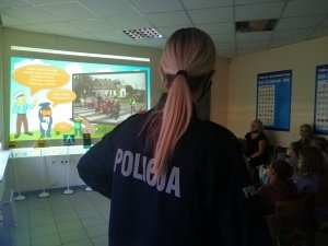 Dzieci oglądają film, widać stojącą policjantkę