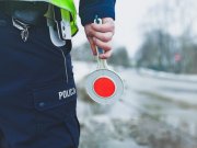 Policjant trzyma w ręku tarczę do zatrzymywania pojazdów przy jezdni