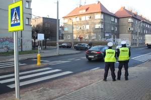 Policjanci stoją przy oznakowanym przejściu dla pieszych, nadjeżdżają pojazdy