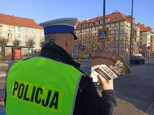 Policjant przy przejściu dla pieszych trzyma ulotki