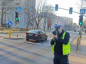 Policjant stoi przy jezdni i dokonuje pomiaru prędkości jadącego samochodu