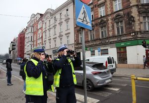 Policjantka przy przejściu dla pieszych robi zdjęcie, a policjant patrzy przez lornetkę