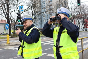 Policjanci ruchu drogowego przy przejściu dla pieszych mierzą prędkość i patrzą przez lornetkę