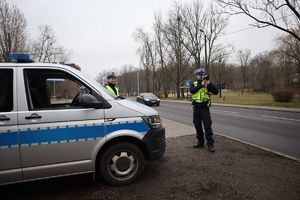 Radiowóz stoi przy jezdni, a policjant ruchu drogowego dokonuje pomiaru prędkości