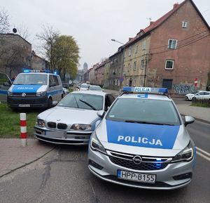 Przy ulicy dwa radiowozy, a pomiędzy nimi samochód marki BMW