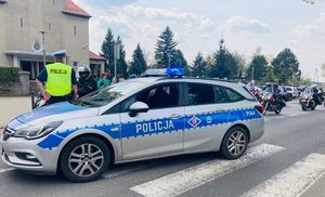 Policjant stoi przy radiowozie zabezpiecza przejazd motocykli