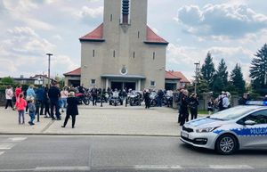 Radiowóz zaparkowany przy jezdni widać motocyklistów i kościół