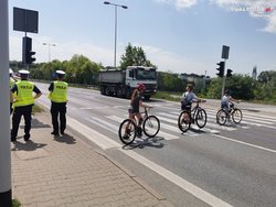 Policjanci przy przejściu dla pieszych, po którym przechodzą piesi z rowerami.