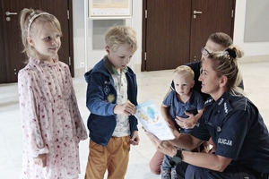 Policjantka rozdaje dzieciom kolorowanki i książeczki