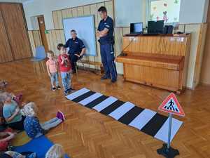 Dzieci stoją przed imitacją przejścia dla pieszych przyglądają się policjanci