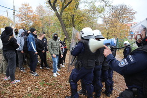 Grupa osób, policjanci i policjant mówiący przez megafon.