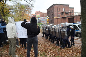 Tłum osób i szyk policjantów wyposażonych w tarcze.