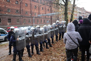 Policjanci z tarczami w szyku oraz widoczny tłum.