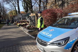 Policjantka stoi przy radiowozie przy cmentarzu.