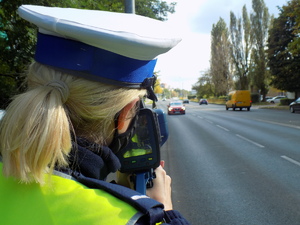 Na zdjęciu widoczna policjantka ruchu drogowego, która dokonuje pomiaru prędkości nadjeżdżającego samochodu.