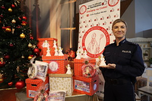 Policjantka trzyma w dłoniach świątecznego aniołka przy choince i prezentach.
