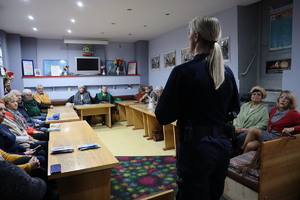 Zdjęcie przedstawia policjantkę, która jest na spotkaniu z emerytami.