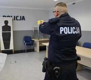 Zdjęcie przedstawia policjanta, który oddaje strzał do tarczy z Tasera.