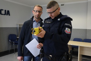 Zdjęcie przedstawia policjanta, który w obecności instruktora sprawdza paralizator elektryczny typu taser.