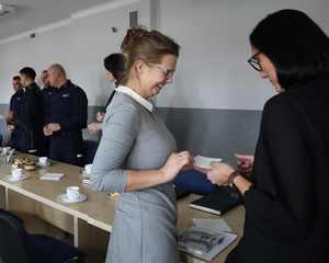 Na zdjęciu widzimy pracowników służby cywilnej, którzy dzielą się opłatkiem, w tle widoczni policjanci.