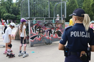 Na zdjęciu widzimy policjantkę w skateparku i dzieci jeżdżące na wrotkach.