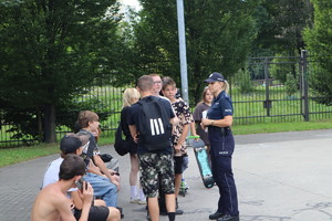 Na zdjęciu widzimy, jak policjantka rozmawia z grupą młodzieży w skateparku.