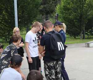 Zdjęcie przedstawia grupę młodzieży i policjantkę, która rozdaje broszury na temat bezpieczeństwa w skateparku