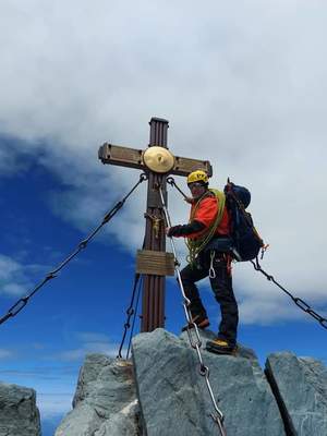 Na zdjęciu widzimy mężczyznę stojącego na szczycie góry przy krzyżu.